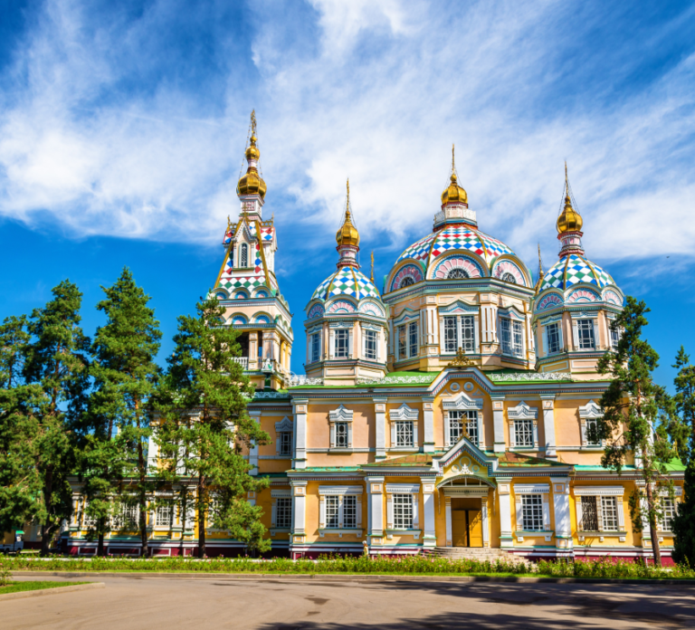 Colorful domes and intricate architecture of Ascension Cathedral in Panfilov Park, Almaty, Kazakhstan under a blue sky.