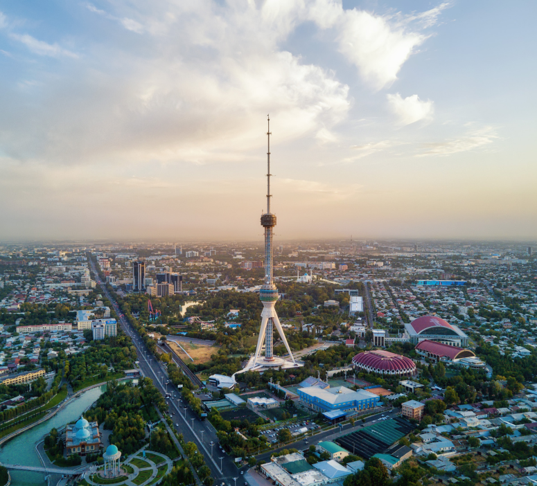 Aerial view of the iconic Tashkent TV Tower bathed in sunset hues, surrounded by the sprawling cityscape of Tashkent, Uzbekistan.