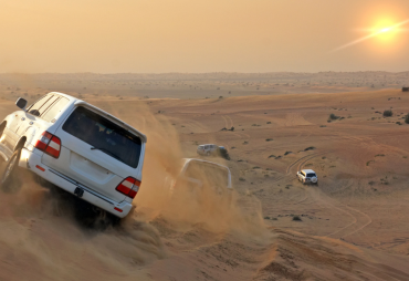 Off-road vehicles navigating the undulating dunes of the Dubai desert during a sunlit safari.