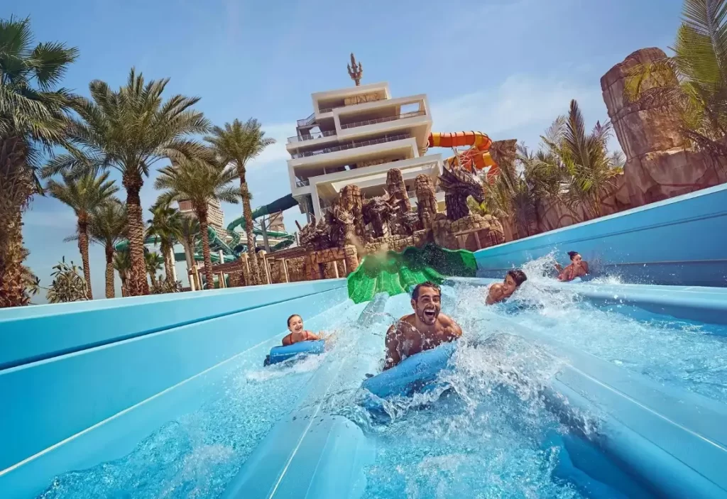Visitors having a blast sliding down a water slide amidst palm trees and thematic sculptures at Atlantis Aquaventure.