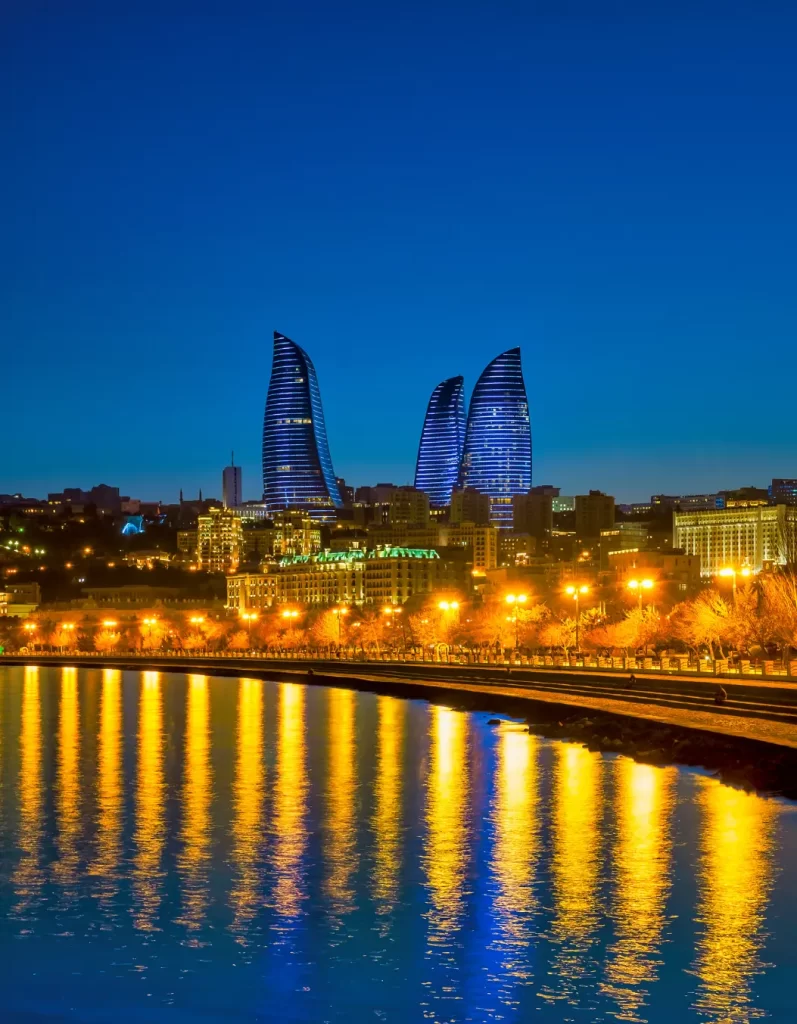 Nighttime skyline of Baku, Azerbaijan, highlighting the illuminated Flame Towers reflecting on the tranquil waters.