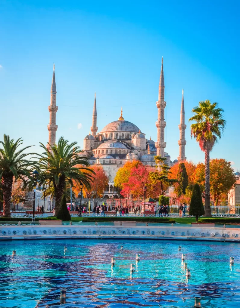 Iconic Blue Mosque with its towering minarets, set against a blue sky, reflecting in the waters of a nearby fountain in Istanbul, Turkey.