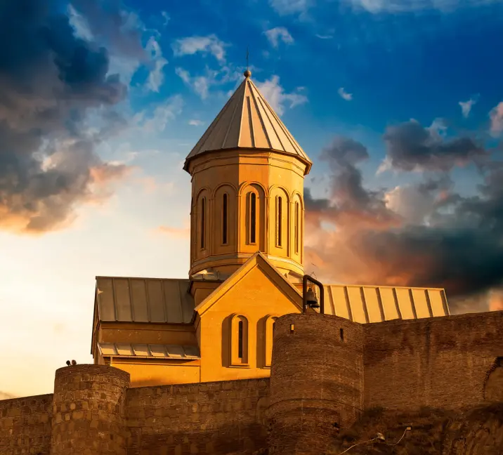 Stunning sunset over the historic Tbilisi church tower, with a dramatic clouded sky backdrop.