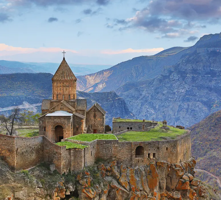 Scenic view of Tatev Monastery perched on a cliff with Armenia's rugged mountains in the background.