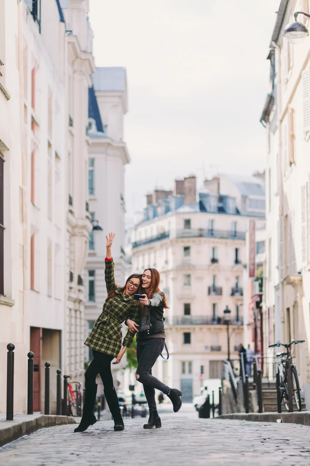 Two joyful friends capturing a selfie on a picturesque Parisian street, embodying the spirit of travel and friendship.